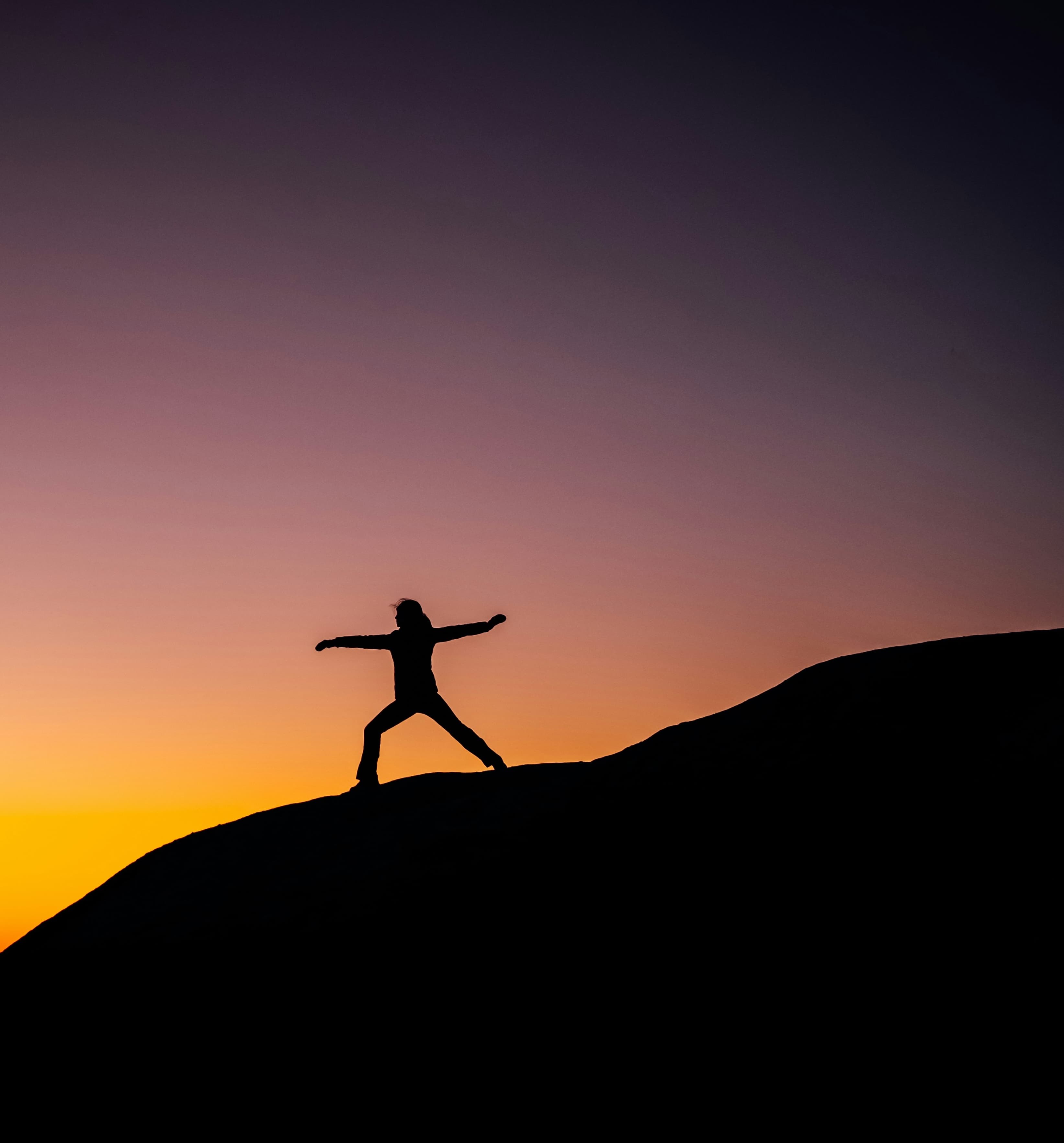 Silhouette of person with arms outstretched against orange sunset sky, conveying health and vitality